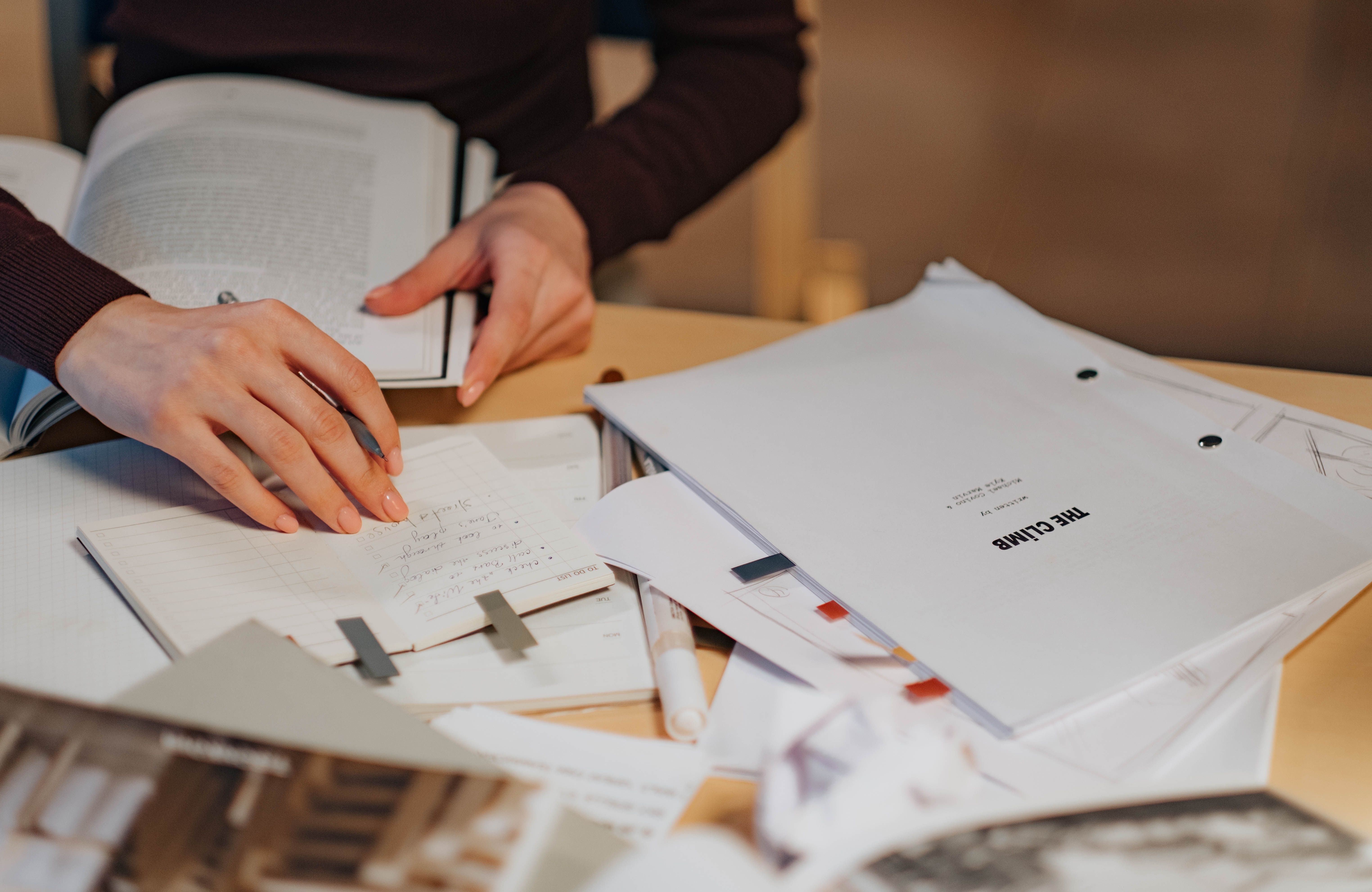 Hands annotating a research notebook beside academic papers and a laptop